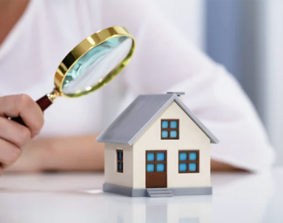 A person with a magnifying glass looking at a miniature home simbolyzing property title search